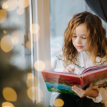 child reading a book by the christmas tree