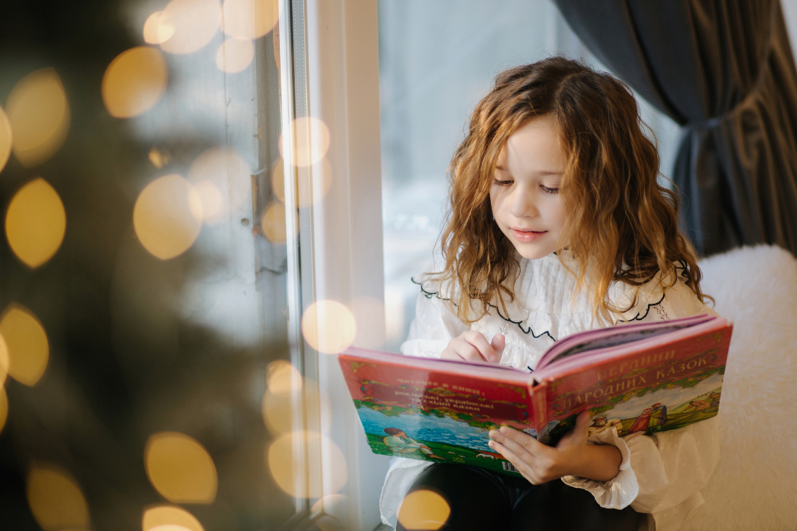 child reading a book by the christmas tree